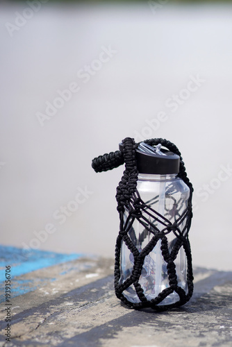 Clear water bottle with black macrame cover on wooden dock