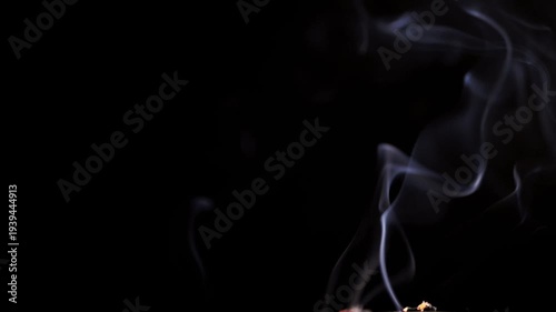 Thin wisps of white smoke gracefully curl and billow before fading into a dark background. Concept of magical atmosphere, spiritual meditation, and abstract floating vapor forms. Slow motion.