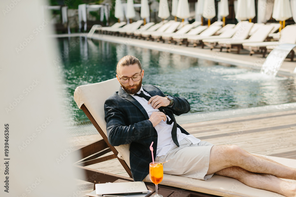 Fototapeta premium Businessman relaxing by the pool after work, loosening his tie