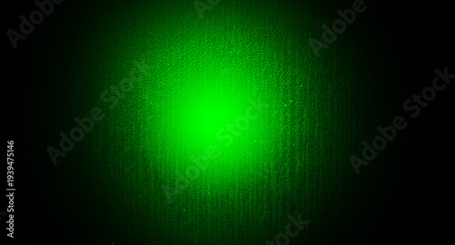 Green spotlight on dark textured wall background with vignette