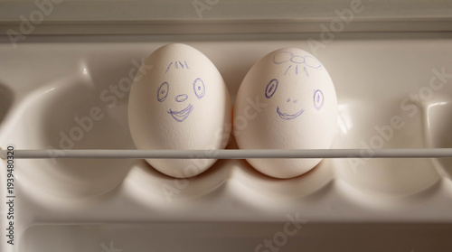 Two eggs with funny faces painted on them are on the refrigerator shelf