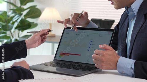 Business people discussing sales charts on a laptop screen during a meeting in a bright modern office.