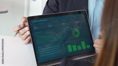 Business colleagues discussing carbon neutral dashboard and sustainability metrics on a laptop during an office meeting.