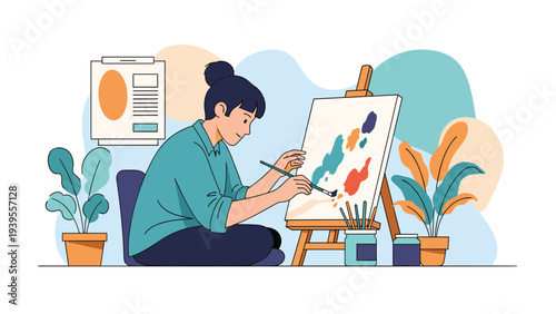 Young woman artist sitting on the floor in her studio and painting colorful abstract shapes on a canvas using a paintbrush and palette.