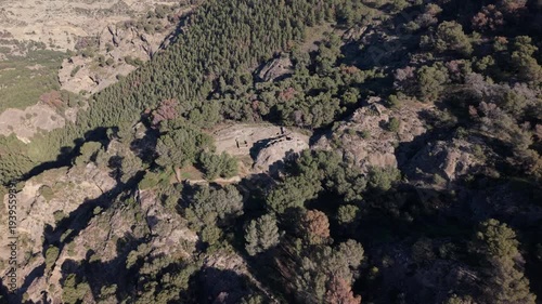 Aerial shot of the ruins of the Mozarab castle of Bobastro, located on a rocky plateau in the hills near El Chorro, Spain. The drone reveals the stone remains of the fortress surrounded by trees