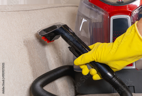 Gros plan sur une personne avec un gant jaune en train d'utiliser une shampouineuse. La machine sert pour le nettoyage de tissus d'ameublement.