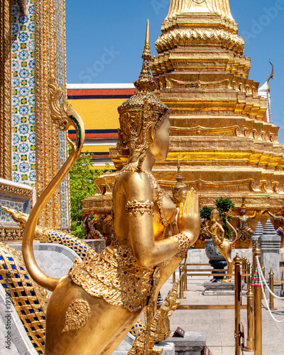 Elaborate gold statues at Wat Phra Kaeo in Bangkok next to the Thai Royal Palace under a blue sky