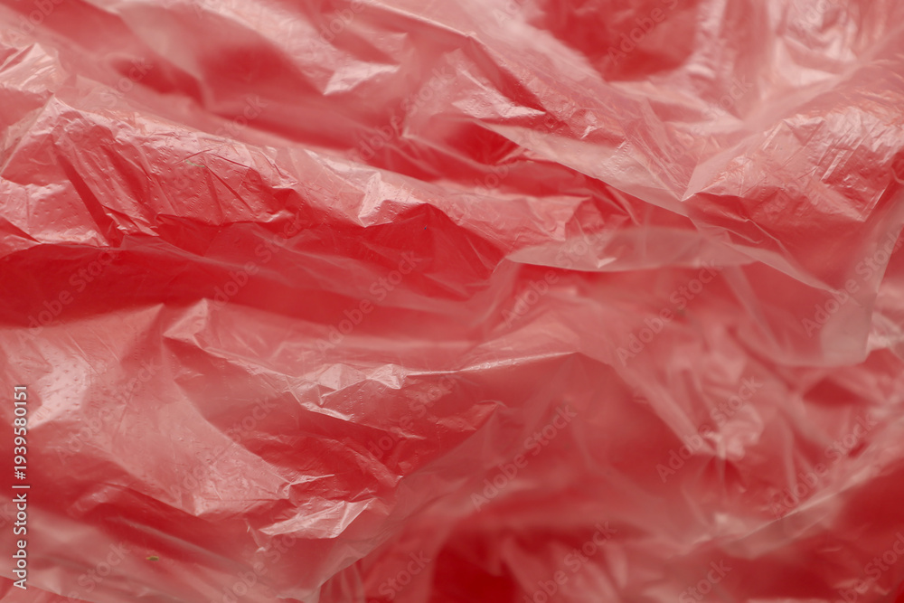 Fototapeta premium ​A macro shot demonstrates the complex abstract texture of a thin red plastic bag with numerous wrinkles and creases. The detailed polyethylene surface creates a play of light and shadow, highlighting
