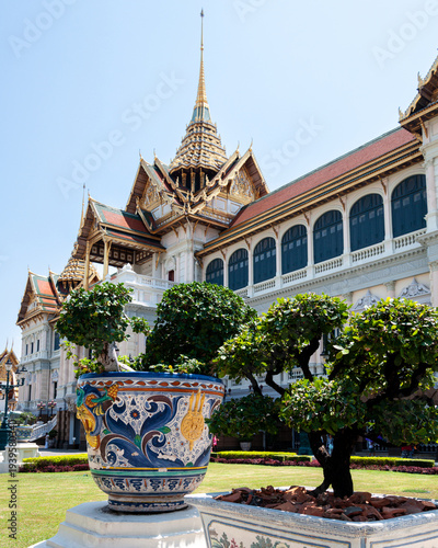 A portrait style photo of the Thai Royal Palace, Bangkok behind a large brightly coloured ceramic pot with greenery