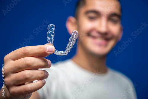 Young man holding a clear removable aligner, showing modern orthodontic treatment for teeth straightening and dental health