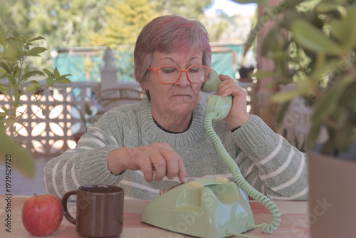 Mujer mayor con gafas llamando con un teléfono de disco antiguo de color verde