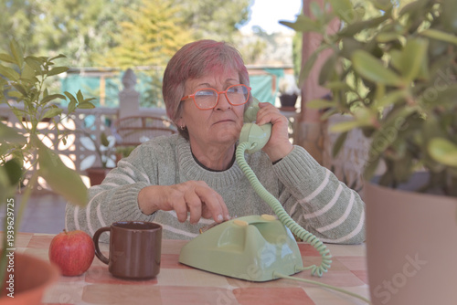 Mujer mayor con gafas llamando con un teléfono de disco antiguo de color verde