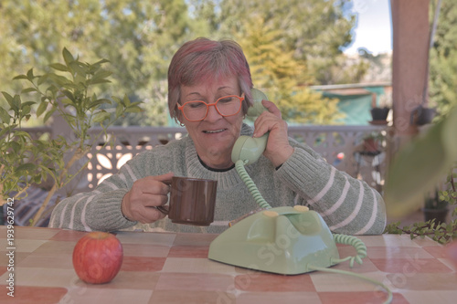 Mujer mayor con gafas llamando con un teléfono de disco antiguo de color verde