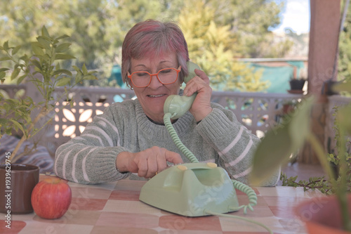 Mujer mayor con gafas llamando con un teléfono de disco antiguo de color verde