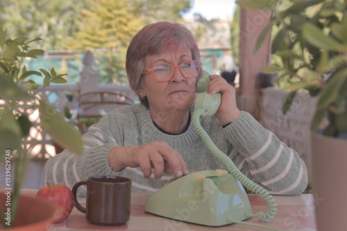 Mujer mayor con gafas llamando con un teléfono de disco antiguo de color verde
