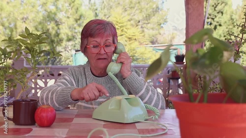Mujer mayor con gafas llamando con un teléfono de disco antiguo de color verde