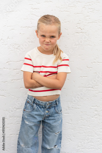 young girl with grumpy facial expression and arms crossed, wearing striped shirt and blue jeans