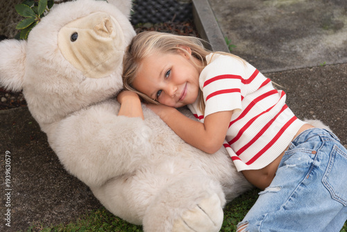 little smiling girl leaning against her big teddy bear