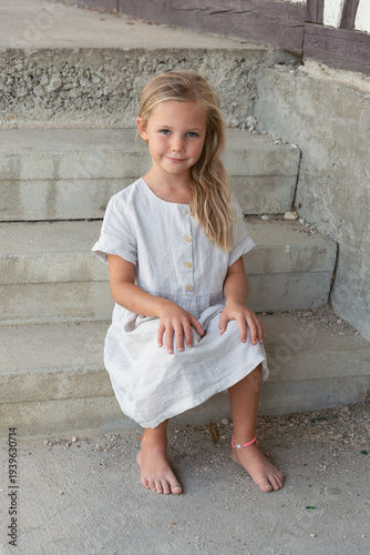 little blonde smiling girl in white dress sitting on stone steps