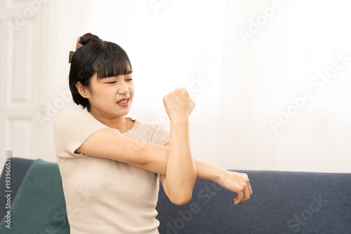 Asian woman stretching her arm and elbow with discomfort. Concept of arm numbness, muscle tension, office syndrome, fatigue, and health care. arm, stretch, numbness, pain, elbow, muscle, tension.