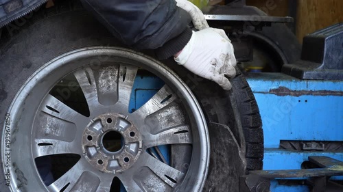 Auto mechanic removing a car tire from wheel rim using tire changing machine in workshop. Car service and vehicle maintenance process.
