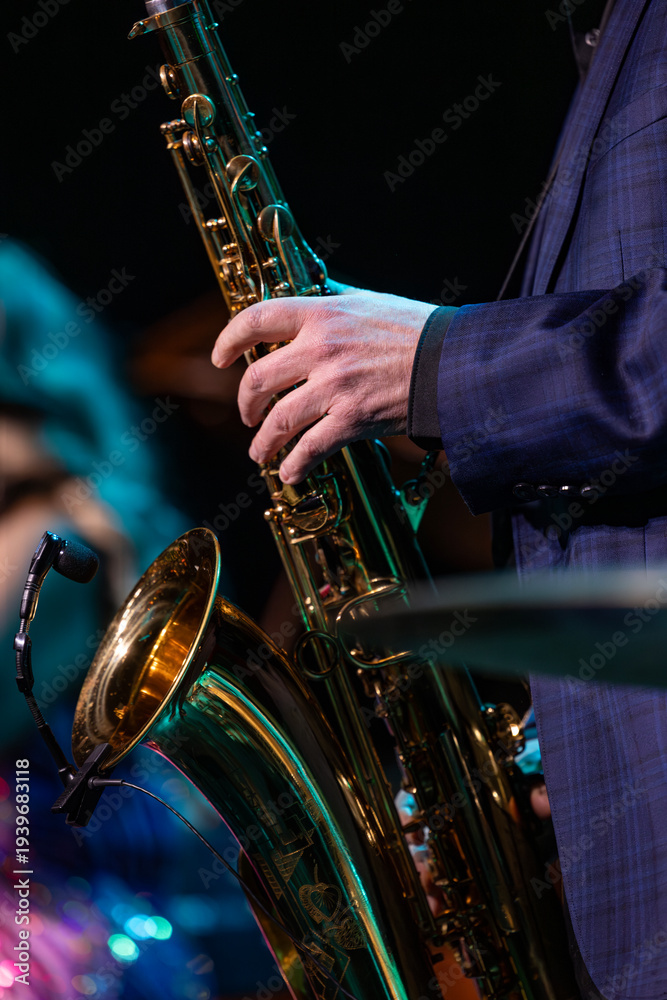 Obraz premium Mans Hands Holding a Saxophone on Stage with a Performer in the Background on Stage