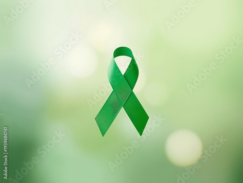 Green awareness ribbon on blurred green background symbolizing hope