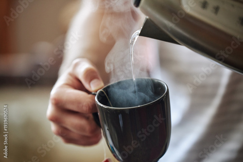 Pouring hot water from kettle into steaming cup