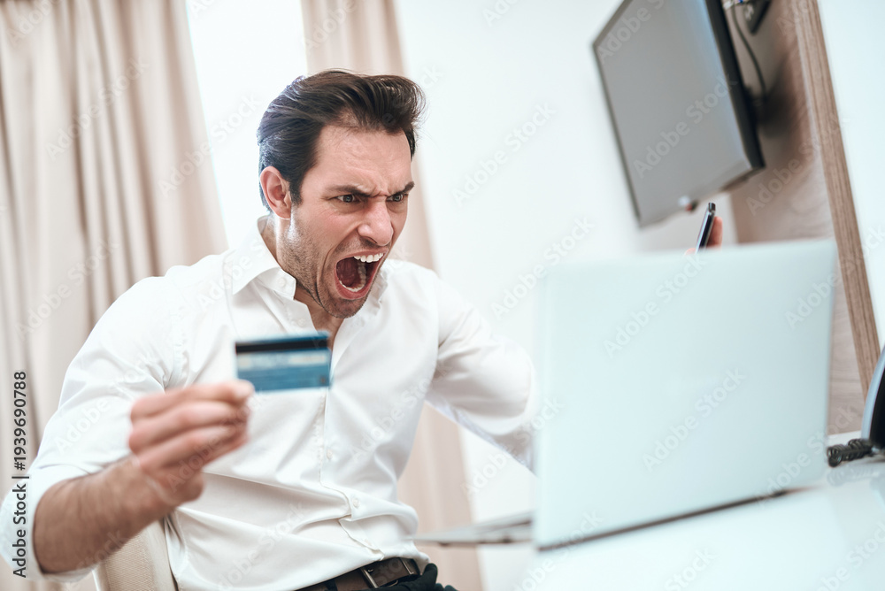 Fototapeta premium Man screaming holding credit card facing laptop