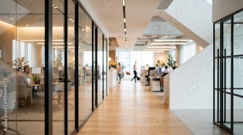 Bright modern glass walled office corridor with wooden floor and blurred employees walking toward windows in warm natural light and plants