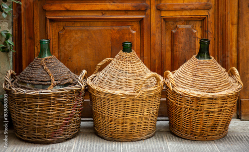 Large glass wine bottles wrapped in willow vines stand near the doors of a wine shop.