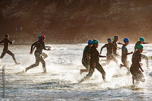 A group of swimmers run into the sea at the start of a competitive race