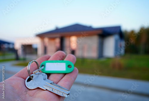 Buying home. Hand holding a bunch of keys at modern private home. Concept of buying real estate, closing a deal, or moving into new home. 