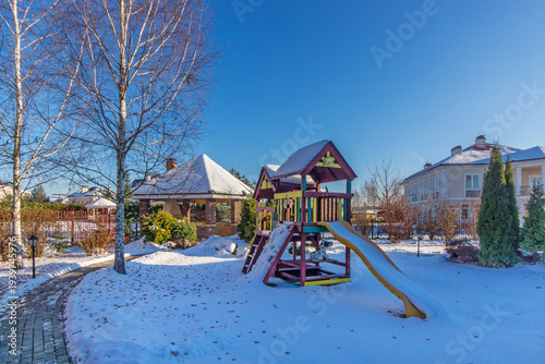Wallpaper Mural Children play on a colorful playground with a slide in a snowy yard. Nearby houses stand under a clear blue sky in winter. The scene is bright and cheerful Torontodigital.ca