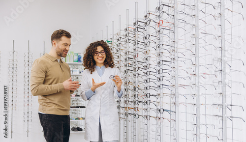 Young female optometrist recommending eyewear to a man in a bright optometry store, improving eyesight