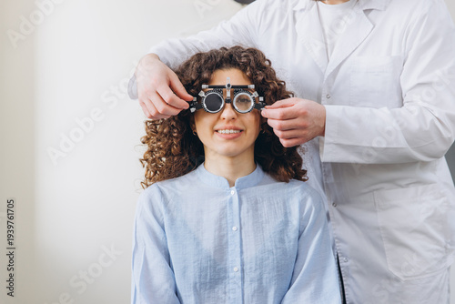 Cuadro en lienzo Woman smiling during eye exam, optometrist adjusting phoropter for vision test,