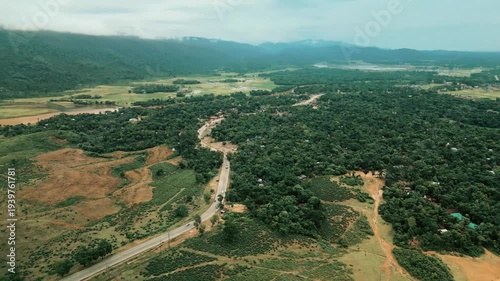 Cinematic drone aerial view of a winding road through lush tea gardens and forest hills in Jaflong, Sylhet, Bangladesh. Peaceful countryside landscape with clouds gathering