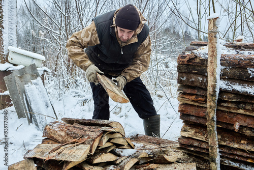 Farmer cut stacked slab lumber into pieces to use as firewood for heating in rural farmhouse.