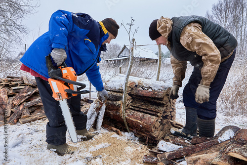 Using chainsaw farmers cut stacked slabwood into pieces for use as fuel in wood stoves.