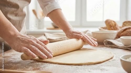 Baker hands using a wooden rolling pin to flatten dough on a floured kitchen table