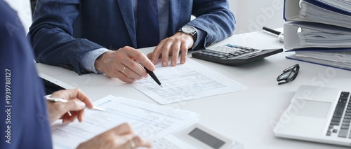 Accountants analyzing financial documents, calculating numbers together at shared workspace with laptop and office supplies surrounding them. Audit and taxes in business