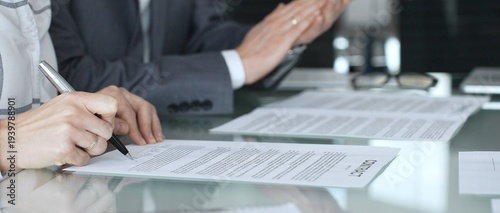 Businesswoman signing contract documents while male colleague is clapping, finalizing successful partnership agreement. Business people concept