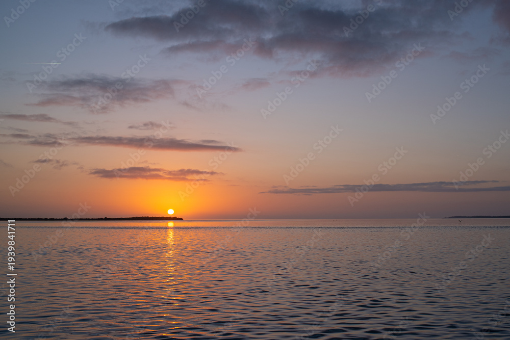 Fototapeta premium Orange sunrise over a calm ocean with an island and clouds in the sky
