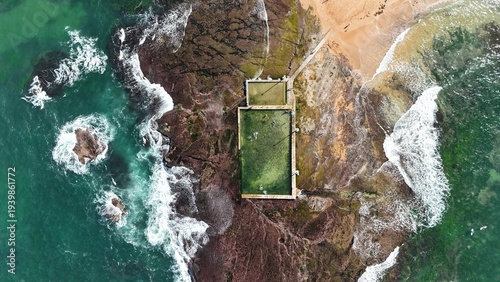 Drone shot aerial view of a beach rock pool and waves crashing over rocks at a beach in Sydney Australia in Summer 