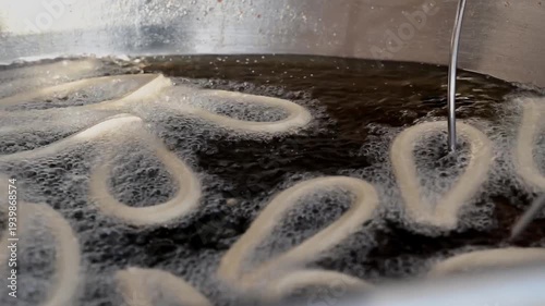  cooking churros and turning them while frying in boiling oil using metal rods inside a professional fryer. Essential equipment in traditional Spanish churrerías