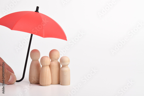 Hand holding a red umbrella protecting wooden family figures isolated on a white background. Family insurance, life protection, financial security, and risk management concept.