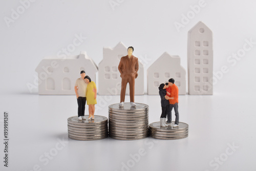 Miniature people standing on stacks of coins with house silhouettes in the background. Wealth distribution, financial inequality, property ownership, and socioeconomic differences in housing.