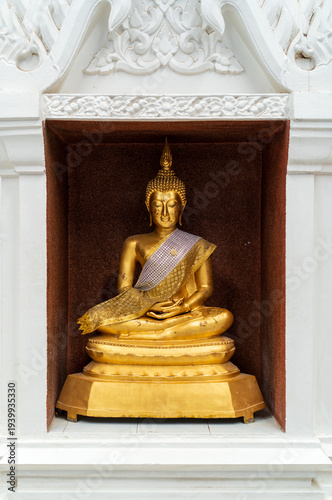 general golden Buddha image in seated meditation posture within white frame found in Thai temples is holy sacred object revered and esteem respect worshipped by Buddhists in Thailand and across Asia