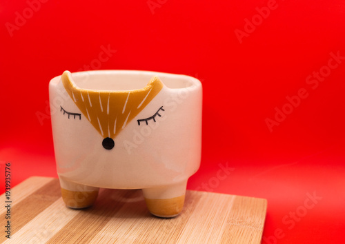 Subject shot of funny ceramic pot made as funny cartoon fox. Bright plant pot for interior design is isolated on the white background.