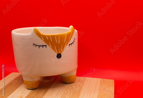 Subject shot of funny ceramic pot made as funny cartoon fox. Bright plant pot for interior design is isolated on the white background.